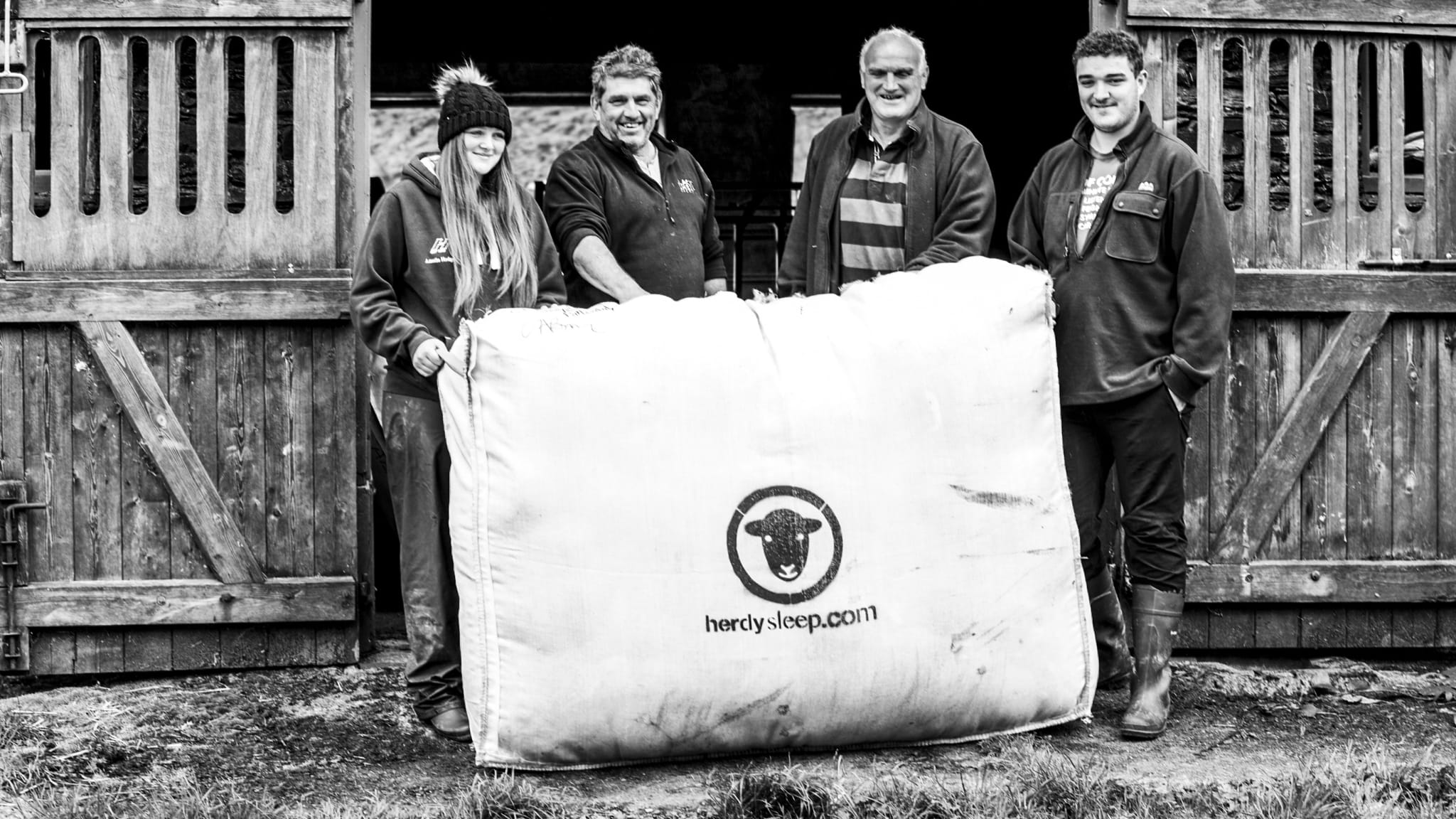 Shepherds and farmers, young and old, hold up a woolsack of Herdysleep fleece