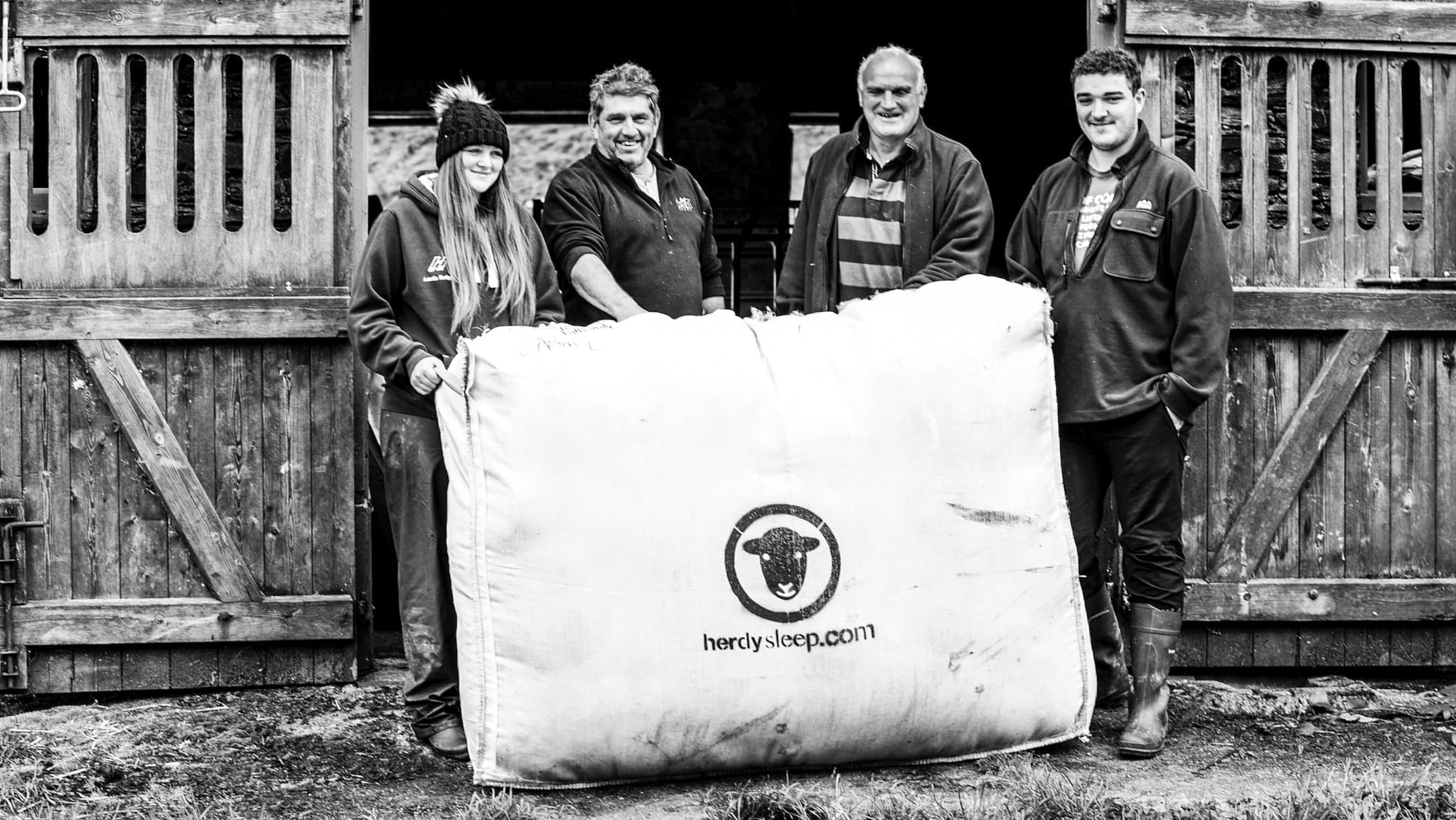 Lake District farmers smile for the camera with a woolsack filled with Herdwick wool. Photo ©Spencer Hannah.